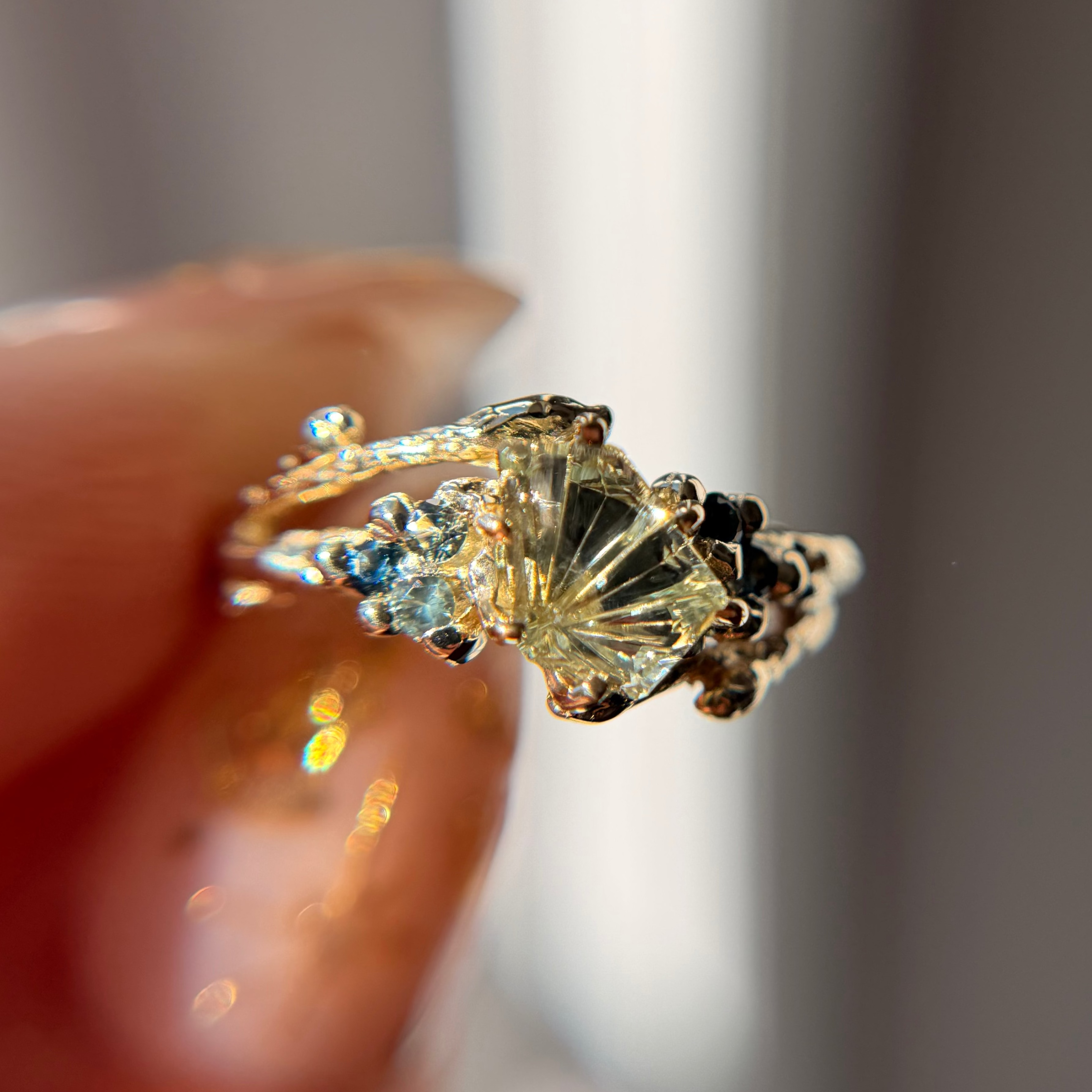Gold ring with a large green gemstone held by a hand against a blurred background